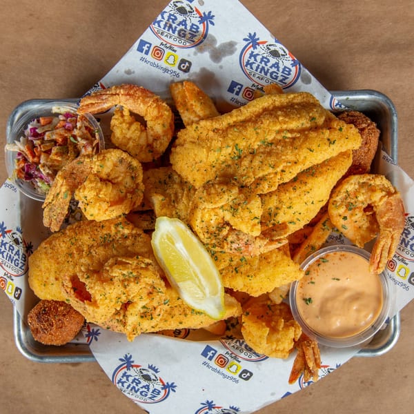 A Krab Kingz seafood platter with fried fish, shrimp, hush puppies, coleslaw, and dipping sauce.