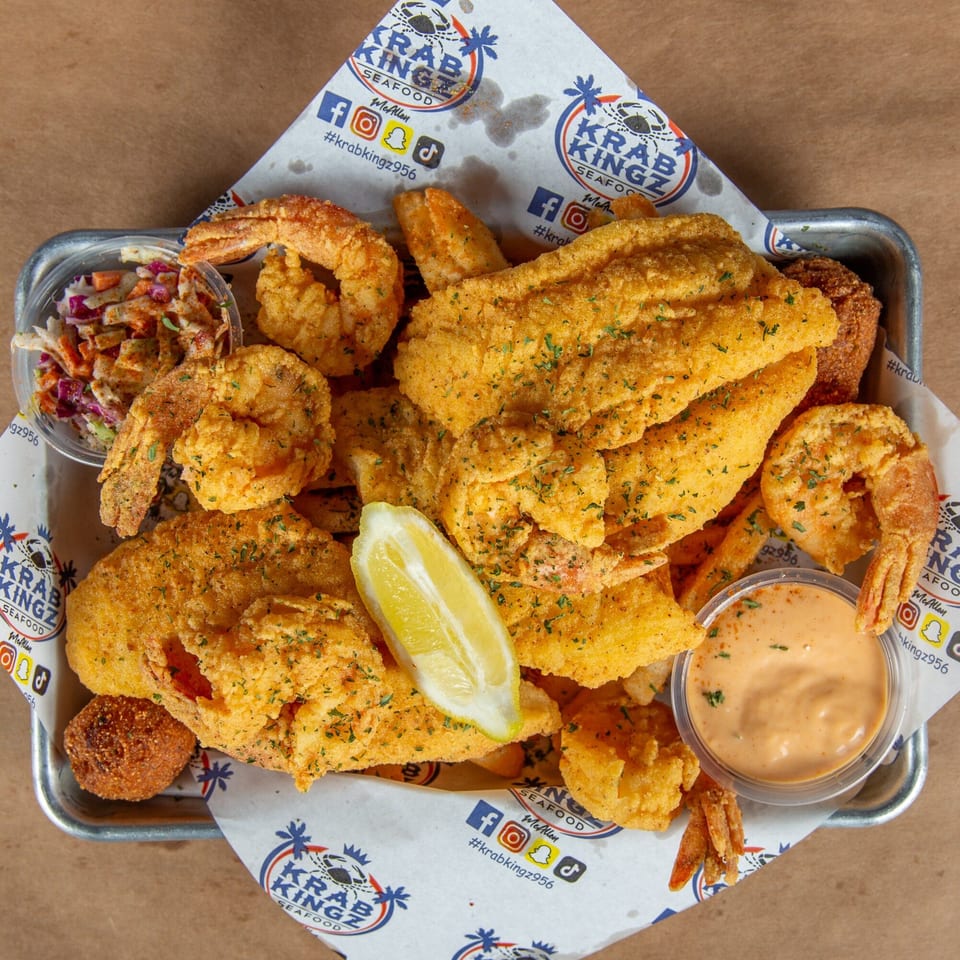 A Krab Kingz seafood platter with fried fish, shrimp, hush puppies, coleslaw, and dipping sauce.