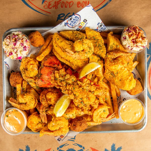 A Krab Kingz seafood platter with fried shrimp, fish, fries, hush puppies, coleslaw, and dipping sauces.