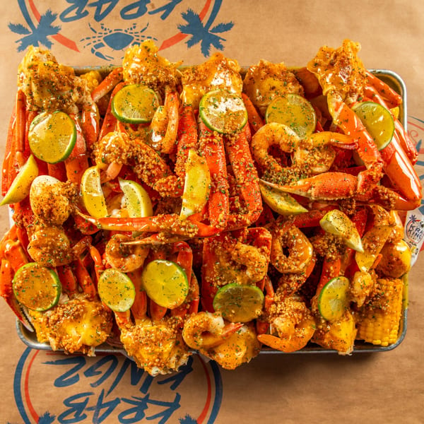 A large platter of Krab Kingz seafood boil with crab legs, shrimp, corn, and citrus slices.