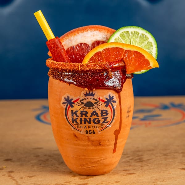 A Krab Kingz michelada in a clay cup, garnished with citrus slices and a chili straw.