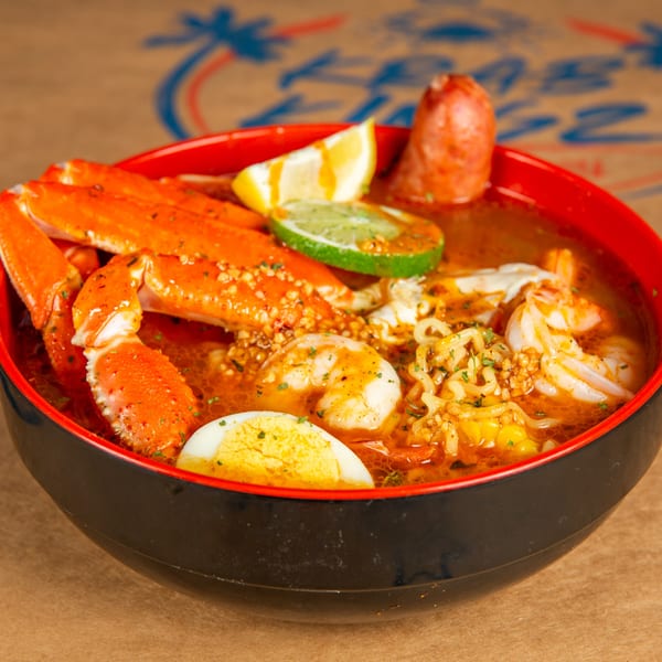 Krab Kingz seafood ramen bowl with crab legs, shrimp, sausage, corn, egg, and lime.