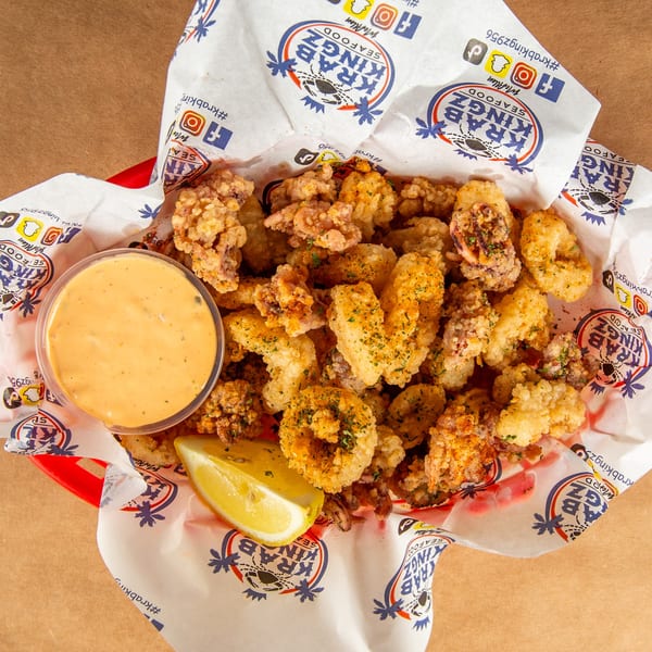 Crispy fried calamari with a side of dipping sauce and a lemon wedge in a Krab Kingz basket.