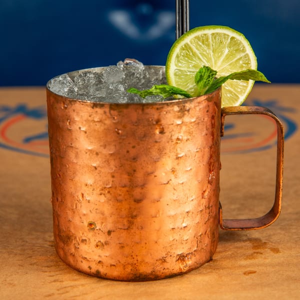 A copper mug filled with ice, garnished with a lime slice and mint leaves.