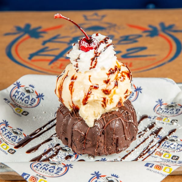 A chocolate bundt cake topped with vanilla ice cream, whipped cream, chocolate syrup, and a cherry.