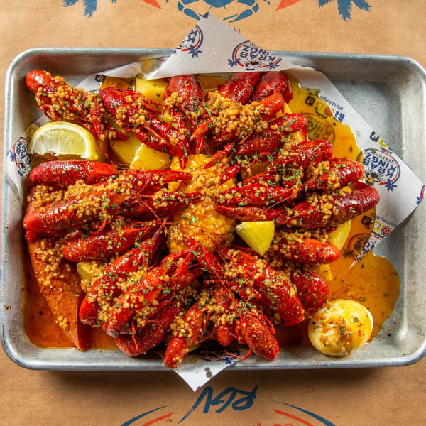 A metal tray filled with Krab Kingz crawfish boil, corn, potatoes, sausage, and lemon wedges.