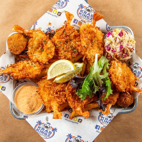 A Krab Kingz seafood platter with crispy fried shrimp, fries, coleslaw, sauce, and lemon wedges.